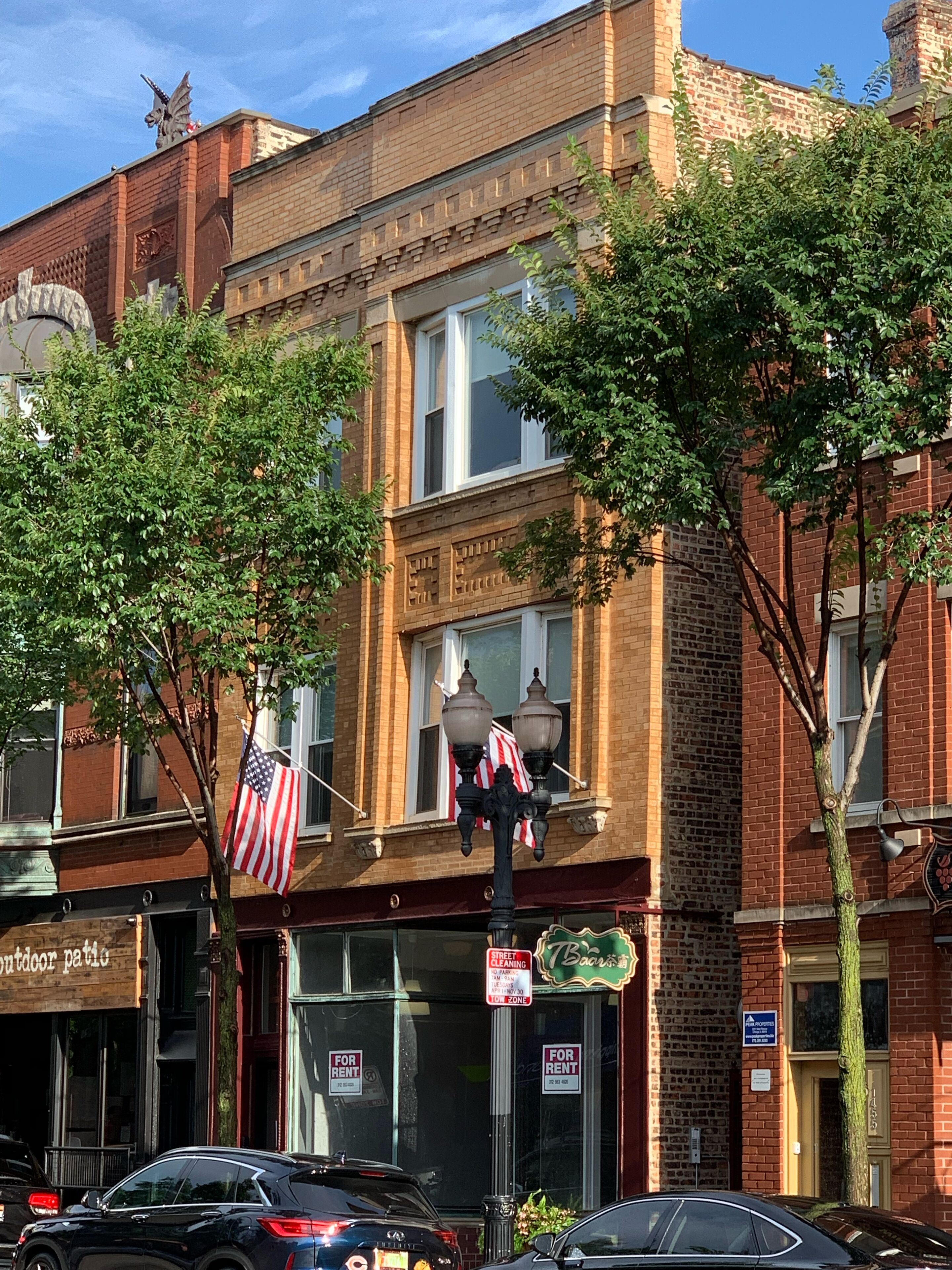 Een tweelaags bakstenen gebouw met een winkelpui, een straatnaambord en een Amerikaanse vlag.
