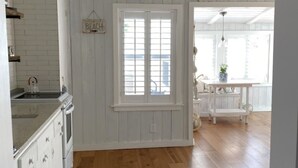A spacious kitchen with wooden floors, white cabinetry, and a large window.
