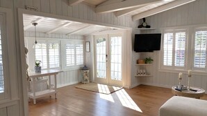 A spacious room with wooden floors, a television mounted on the wall, and a bench.