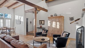 Un salón amplio con un sofá de cuero, dos sillones negros, una mesa de centro de madera y un mueble grande de madera.