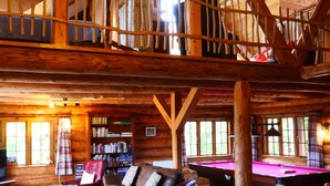 A spacious wooden cabin with a pool table, a cozy seating area, and a balcony with a railing.