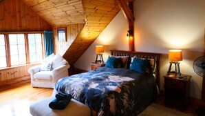 A cozy bedroom with a sloped ceiling, a large bed with floral bedding, a white armchair, and two bedside lamps.