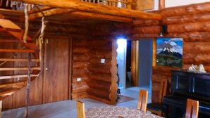 A rustic cabin interior with a dining area, wooden staircase, and a painting on the wall.