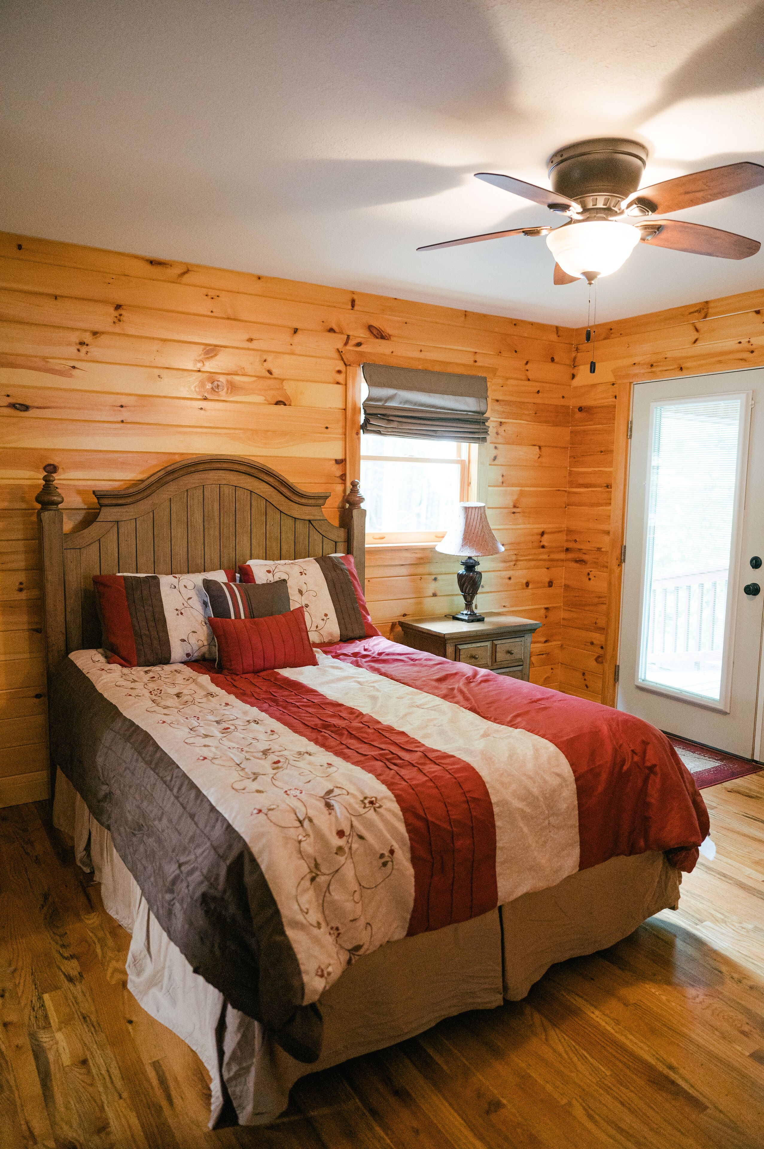 A wooden-paneled bedroom with a bed, a nightstand, a lamp, and a ceiling fan.