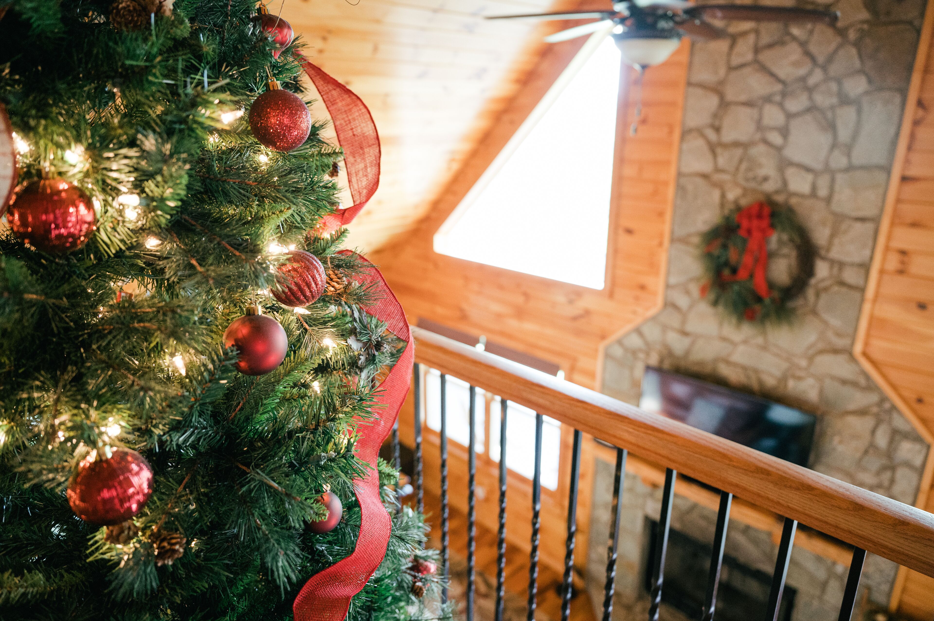 A Christmas tree with red ornaments and lights, a wooden staircase, and a stone wall with a wreath.
