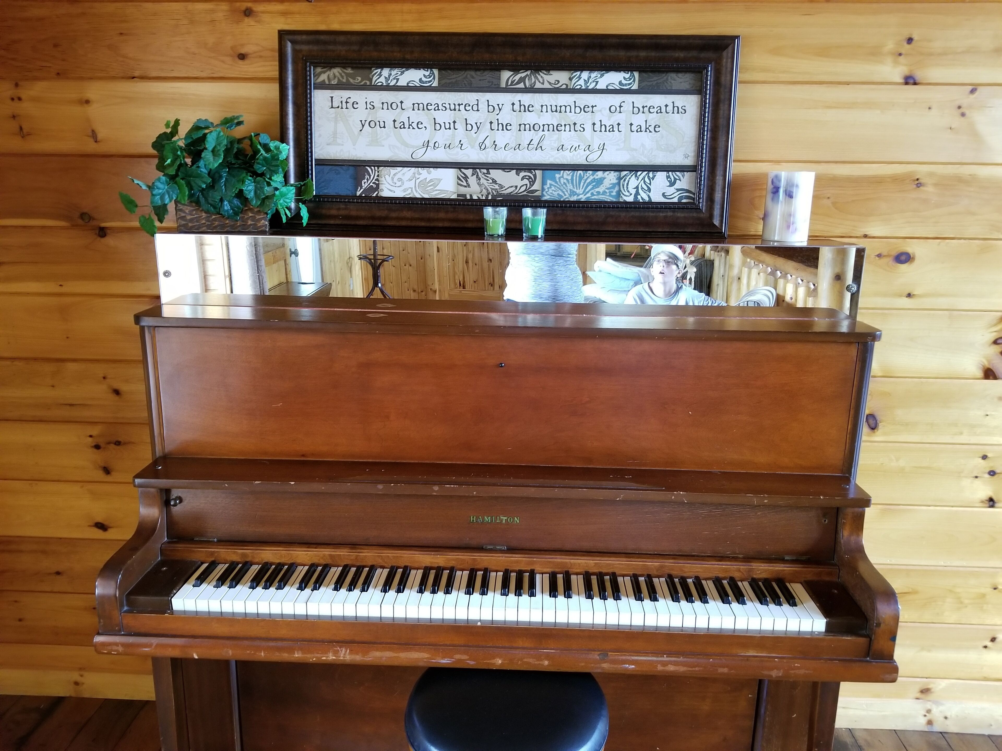 A wooden piano with a framed quote above it.