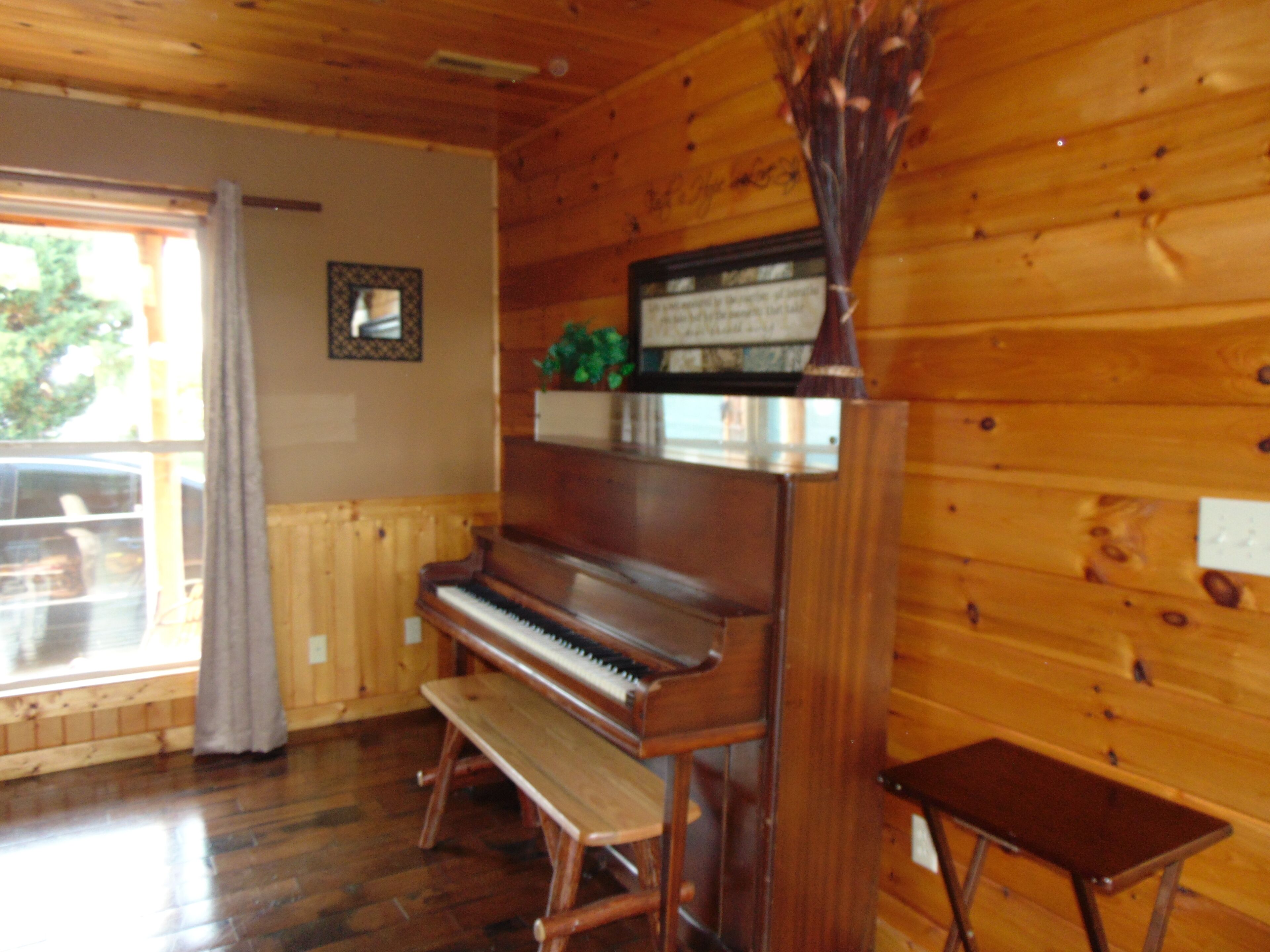 A wooden interior with a piano, bench, and a small table.