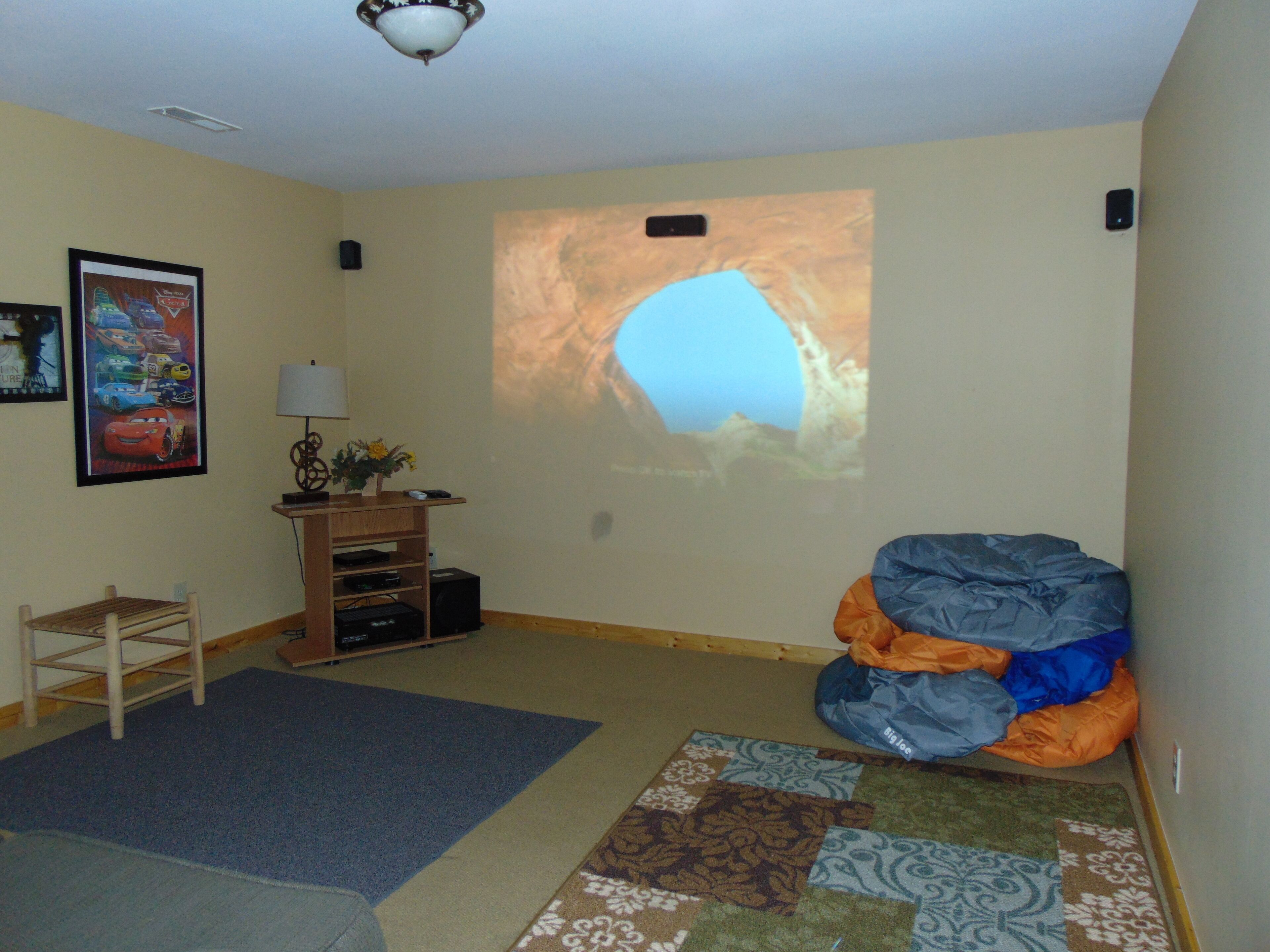Un soggiorno con schermo proiettore, mobile TV in legno, tappeto blu e pouf.