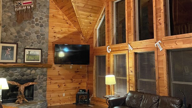 Un interior de madera con chimenea de piedra, sofá de cuero y ventilador de techo.