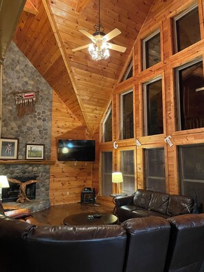 A wooden interior with a stone fireplace, leather sofa, and a ceiling fan.
