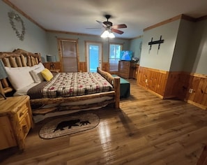 A bedroom with a bed, wooden floor, a ceiling fan, a television, and a wooden dresser.