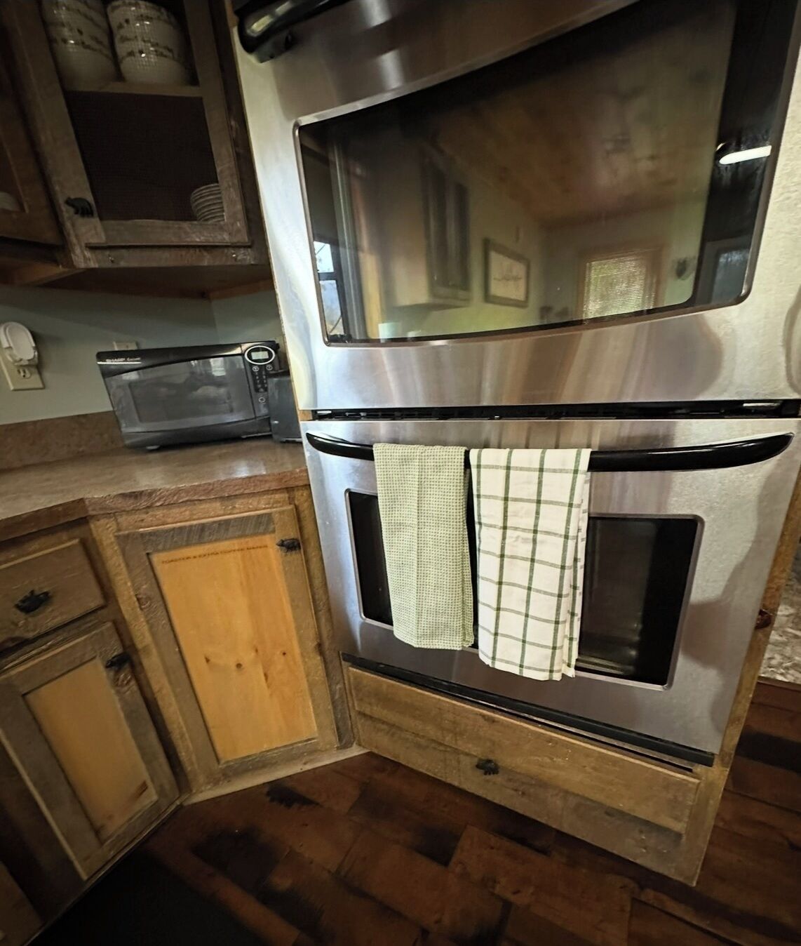 Een keuken met een dubbele oven, een magnetron, houten keukenkastjes en een houten vloer.