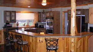 Una cocina con armarios de madera, una isla central con taburetes de bar y vistas al exterior.