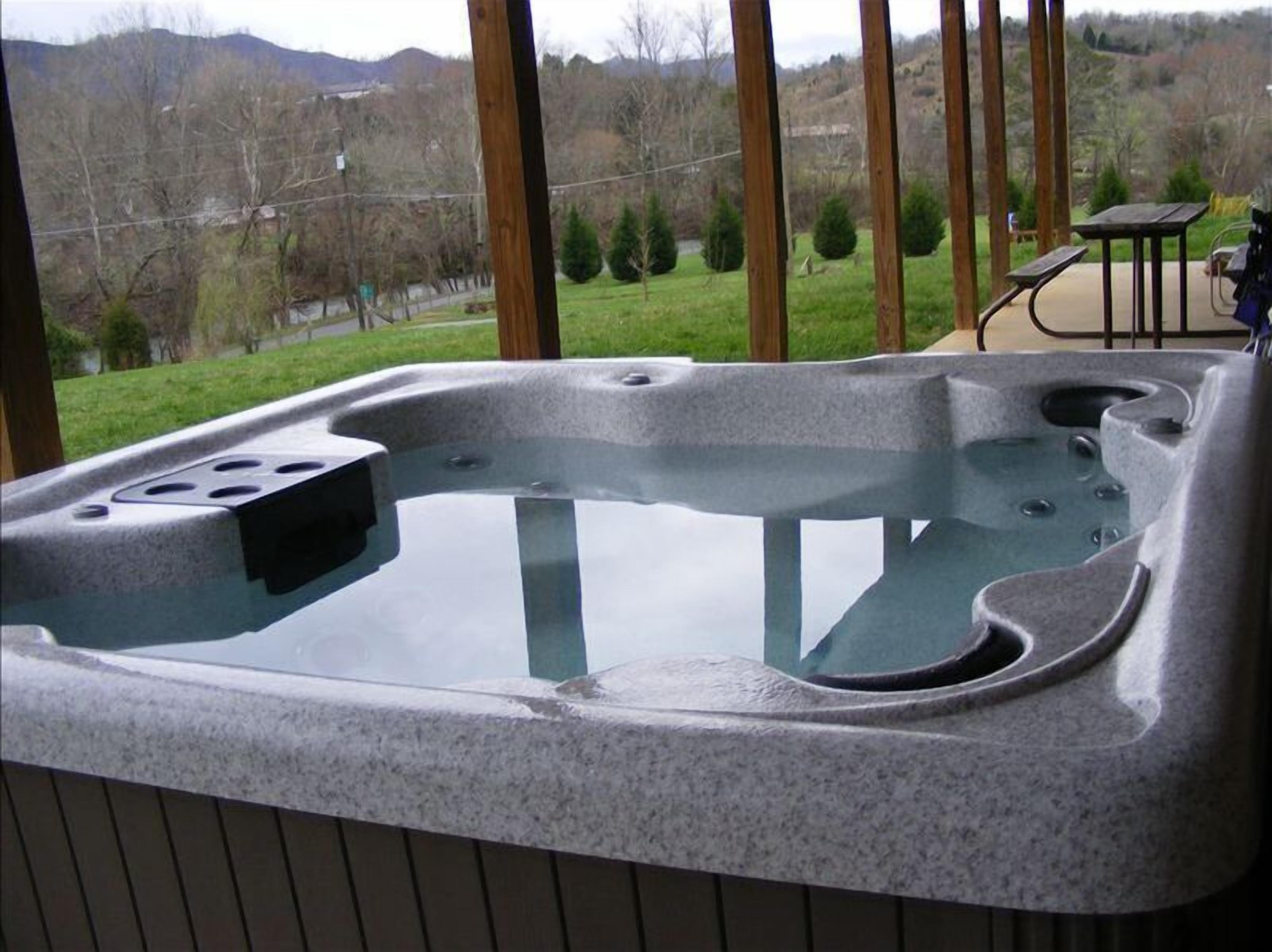 A hot tub with a stone exterior, set on a wooden deck with a view of a green landscape and mountains in the background.