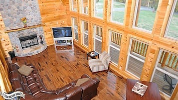 Ein rustikaler Blockhausaustattung mit Kamin aus Stein, Ledersofa, Fernseher und großen Fenstern.