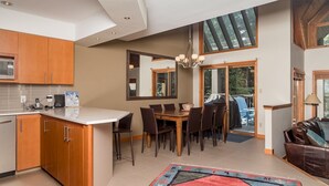 A modern kitchen with wooden cabinets, a dining area with a large table and chairs, and a view of the outdoors through a sliding glass door. - CEDAR RIDGE 17 | Prime Ski-In, Ski-Out Location | Private Garage & Hot Tub (Whistler)