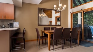 A dining area with a wooden table and chairs, a chandelier, a large mirror, and a view of the outdoors through a sliding glass door. - CEDAR RIDGE 17 | Prime Ski-In, Ski-Out Location | Private Garage & Hot Tub (Whistler)