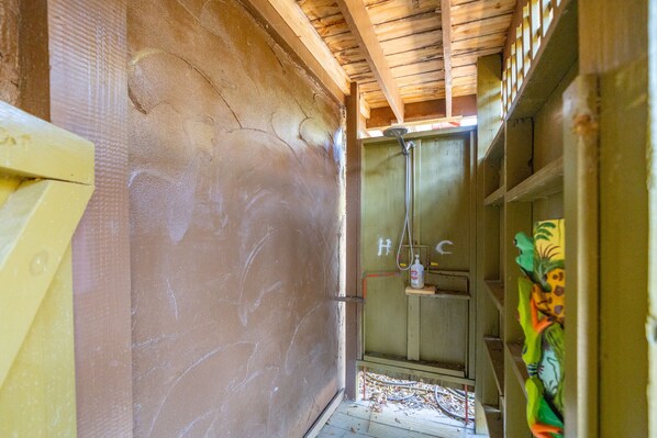 A narrow hallway with a shower area, wooden ceiling, and a door with a handle.