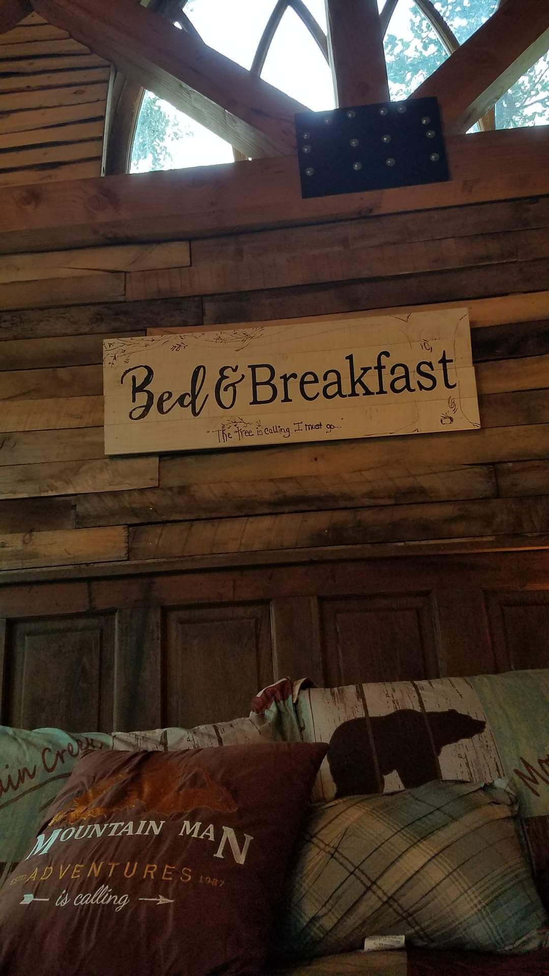 Un cartello con su scritto 'Bed & Breakfast' e una citazione: 'L'albero chiama, devo andare'. Ambiente rustico da baita.
