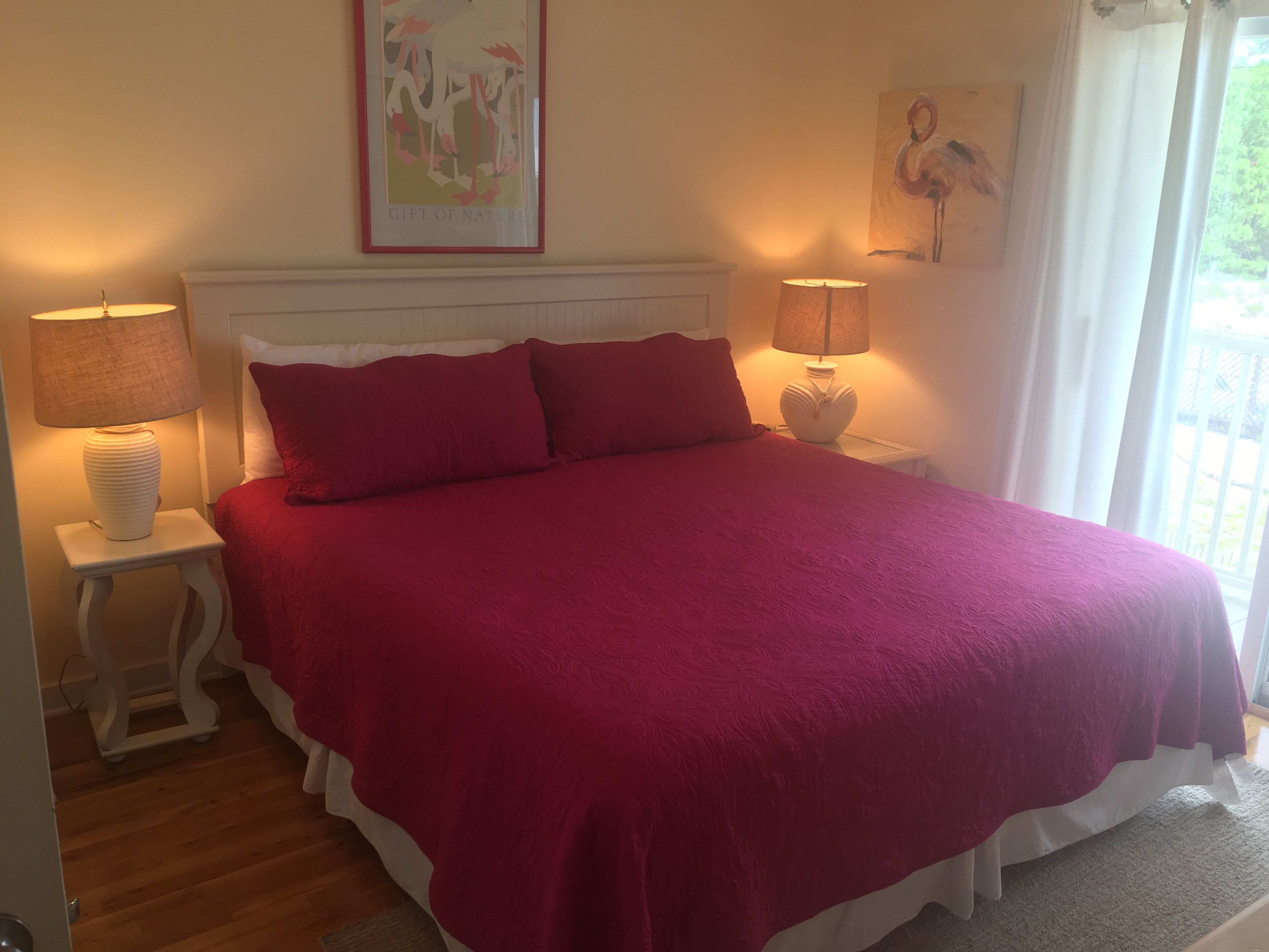 A bedroom with a large bed, two bedside lamps, a framed artwork above the bed, and a window with curtains.