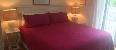 A bedroom with a large bed, two bedside lamps, a framed artwork above the bed, and a window with curtains.