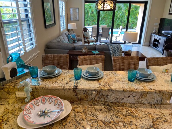 A kitchen with a granite countertop, a dining area with wicker furniture, and a view of a pool and outdoor seating.