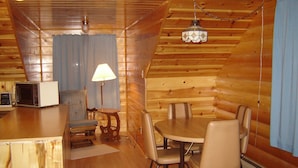 A cozy cabin interior with a wooden dining table, four chairs, a lamp, and a microwave. - Martins Vacation Rental Log Cabin (Hungry Horse)