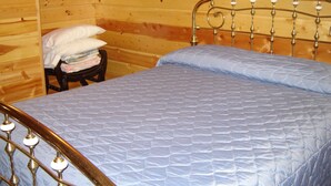 A wooden cabin room with a metal bed frame and a blue quilted mattress. - Martins Vacation Rental Log Cabin (Hungry Horse)