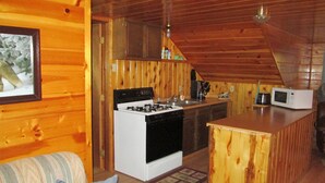 A cozy cabin interior with a kitchen area featuring a stove, sink, and microwave. There is a wooden ceiling and a framed picture on the wall. - Martins Vacation Rental Log Cabin (Hungry Horse)