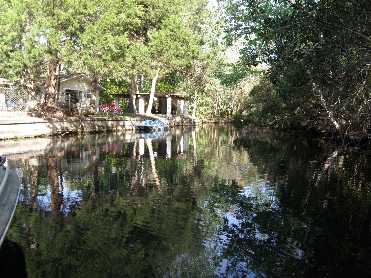 Ein ruhiger Fluss mit einem kleinen Steg und einem Gebäude mit Veranda und roten Stühlen.