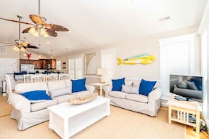 A living room with two white sofas, a coffee table, a TV, and a ceiling fan.
