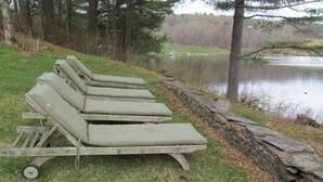 Un hilera de sillones de madera con cojines junto a un muro de piedra frente a un lago.