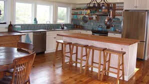 Una cocina con taburetes de madera, una isla central y un refrigerador de acero inoxidable.