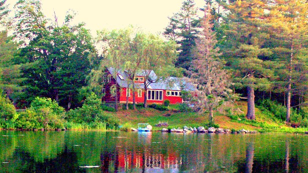 Una cabaña roja junto a un lago rodeado de árboles.
