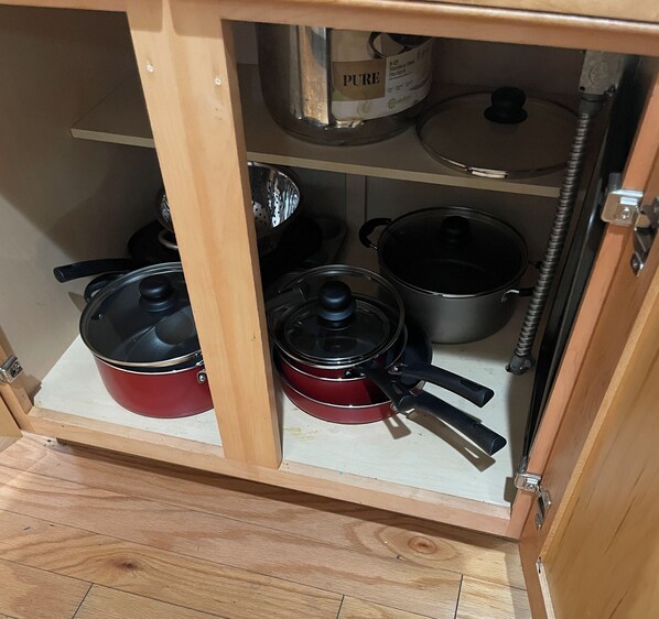 Un armario de cocina con utensilios de acero inoxidable, incluyendo ollas y sartenes.
