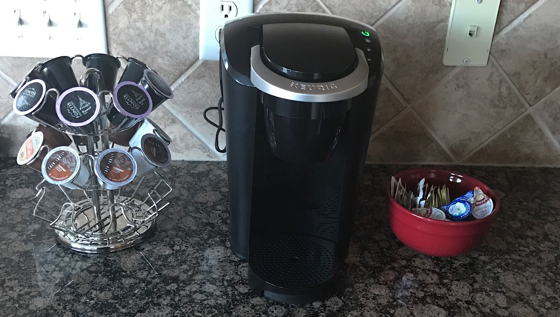 Una cafetera, un portalápices para cápsulas de café, y un recipiente rojo con utensilios sobre una encimera de cocina.