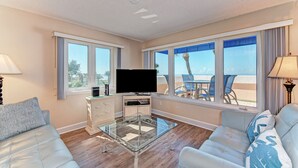 Un salon moderne doté d’un téléviseur à écran plat, d’une table basse en verre et d’un coin salon offrant une vue sur la plage.