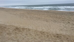 Ein Sandstrand mit sanften Wellen und bewölktem Himmel.