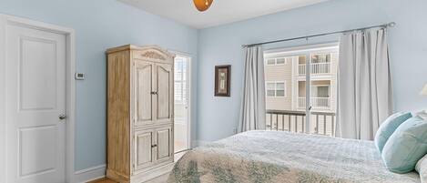 A bedroom with a bed, a ceiling fan, a wardrobe, and a window with a view of a balcony.