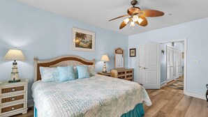 Ein Schlafzimmer mit einem Bett, zwei Nachttischen, einem Deckenventilator und einer Tür zu einem anderen Raum.