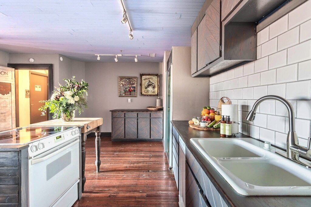 A kitchen with a stove, sink, and wooden cabinets. There is a vase with flowers on the counter and a picture frame on the wall.