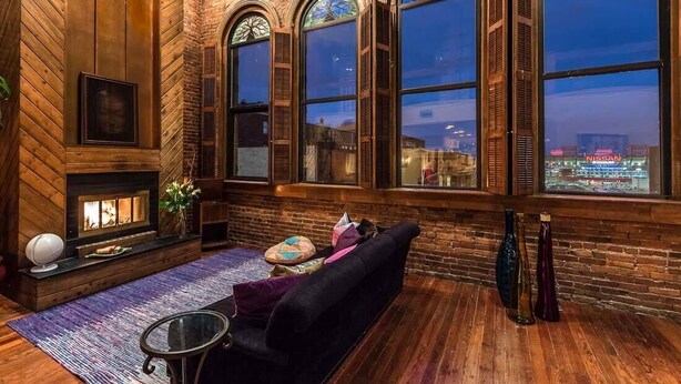 Uma sala de estar acolhedora, com lareira, um sofá e janelas amplas com arcos.