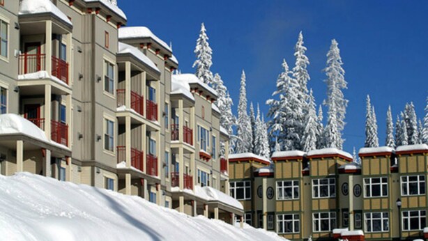 Eine Reihe mehrstöckiger Gebäude mit Balkonen, schneebedeckte Bäume und einem strahlend blauen Himmel.