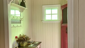 Ein Zimmer mit Holzboden, einem grünen Tisch mit einem Korb, einer roten Tür und einem Fenster mit grünen Glasscheiben.