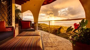 A terrace with a view of the sunset, a sofa, a striped rug, and potted plants. - AMAZING Hillside Home, Private Infinity Pool, Covered Veranda, Spacious Rooms (Manuel Antonio)