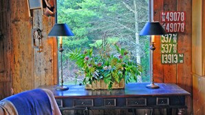 Un intérieur en bois avec une fenêtre donnant sur l’extérieur, deux lampes, un panier en osier rempli de fleurs et un mur décoré de plaques d’immatriculation.