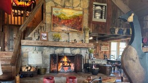 Un intérieur rustique avec une cheminée en pierre, des meubles en bois et une grande sculpture d’oiseau.