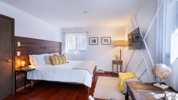 A bedroom with a wooden headboard, a bed with white bedding, a bedside table with a lamp, a globe, and a small plant.