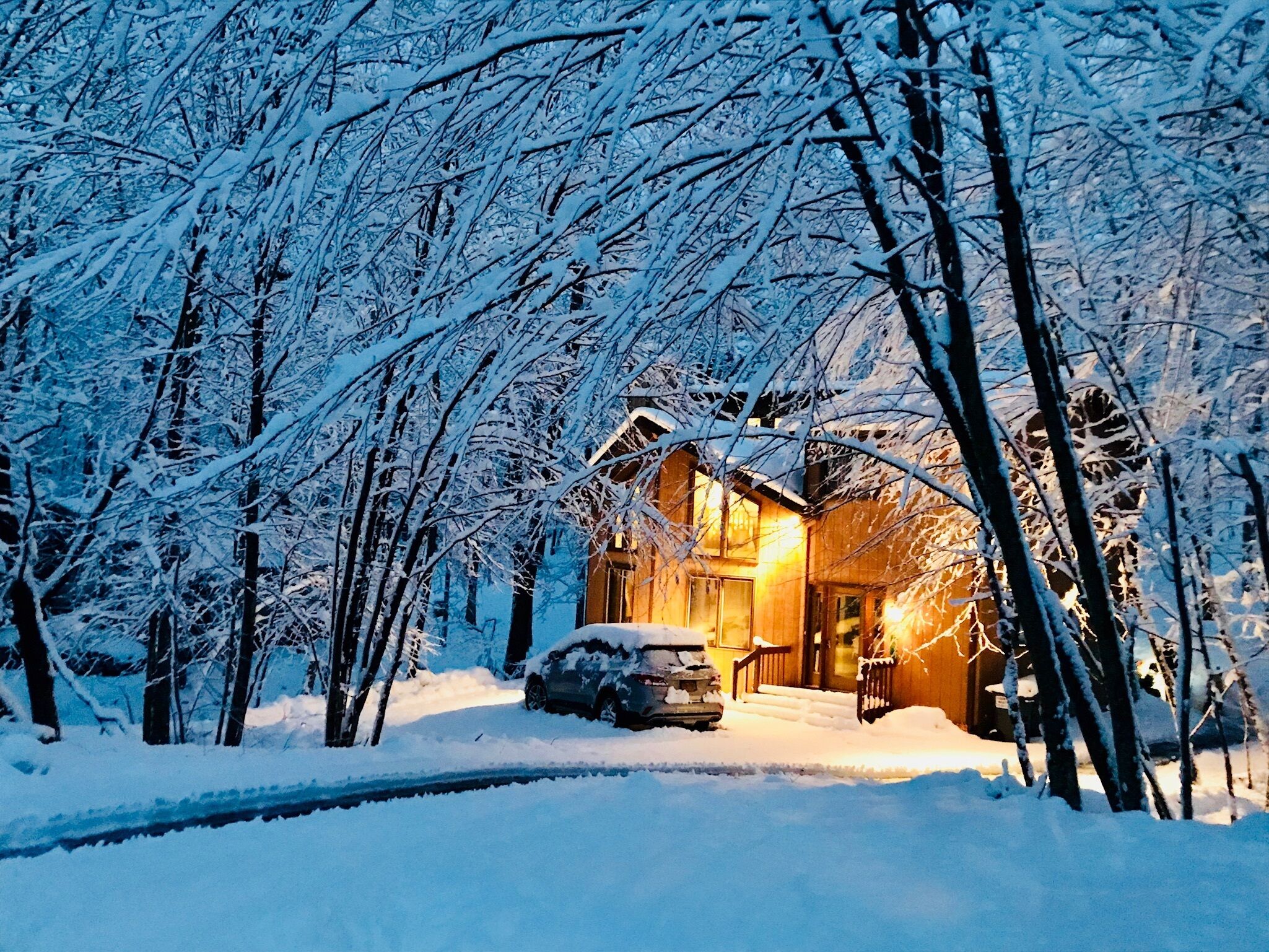 A snow-covered landscape with a wooden cabin and a car parked in front.