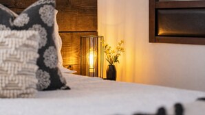 A bed with a patterned pillow, a bedside table with a vase of flowers, and a wall-mounted light fixture.